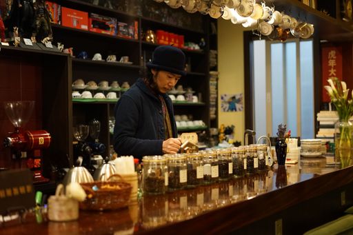An Asian barista making coffee behind a counter in a cafe