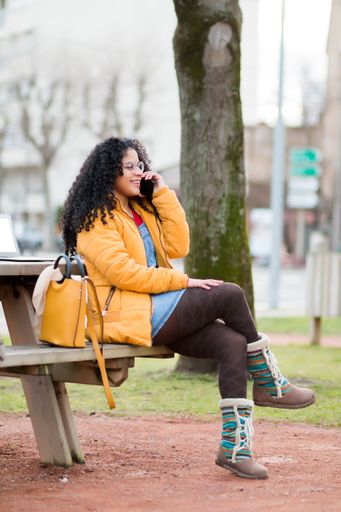 A vertical shot of a woman with curly hair talking on a phone in the park