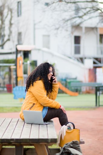 A vertical shot of a woman with curly hair talking on a phone in the park