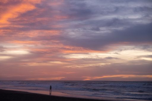 A man is silhouetted against a stunning sunset as he stands at the edge of a beach