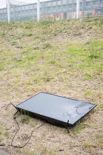 A vertical shot of a broken TV dumped in a grassy field during daytime