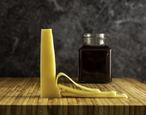 A selective focus shot of partly sliced gouda cheese and a jar on a wooden board
