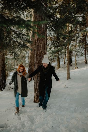 A Beautiful view of a couple wearing warm clothes running and having fun at the snow park