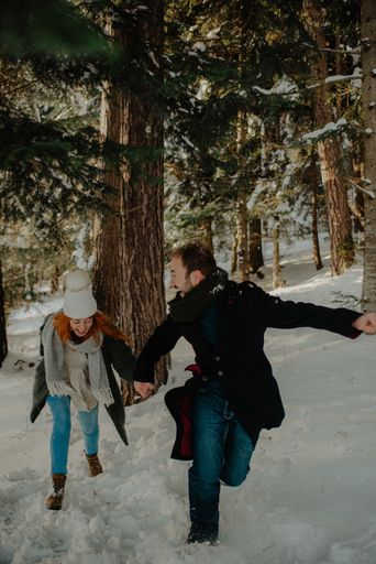 A Beautiful view of a couple wearing warm clothes running and having fun at the snow park