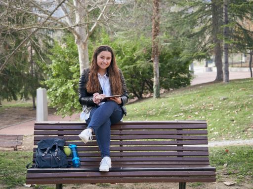 A young caucasian female using her tablet while sitting on a wooden bench in the park