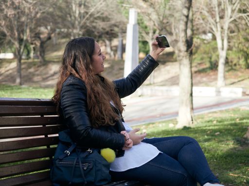 A young female taking a selfie with her smartphone while sitting on a wooden bench in the park