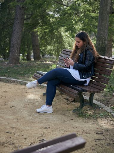 A young caucasian female using her smartphone while sitting on a wooden bench in the park