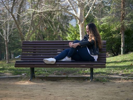 A young caucasian female sitting on a wooden bench in the park