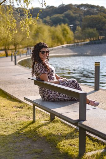 A vertical shot of a young Hispanic female sitting on a bench in a park