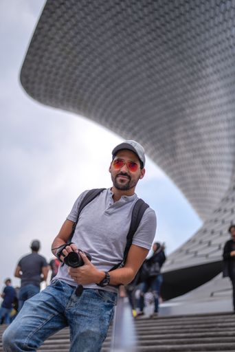 A young man holding camera in his hand in the front of Soumaya museum in Mexico city.