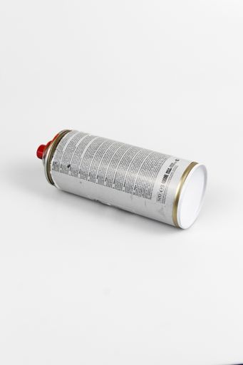 A vertical shot of a spray paint lies on a white surface with a white color in the background