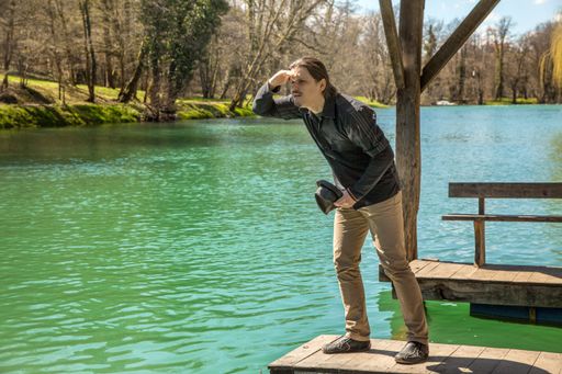 A closeup shot of a male standing on the wooden pier near the lake and looking at the horizon