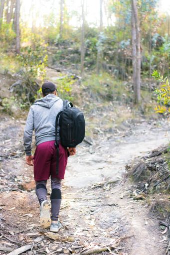 A back view of a sportsman walking with a black backpack after finishing the workout in nature
