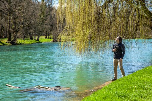A male standing on the shore of the lake with closed eyes and enjoying the light of the sun