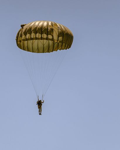 A vertical aerial view of a man flying on a yellow parachute in blue sky