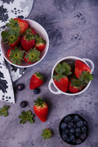 Strawberries and blueberries presented in white bowls, on a gray background.