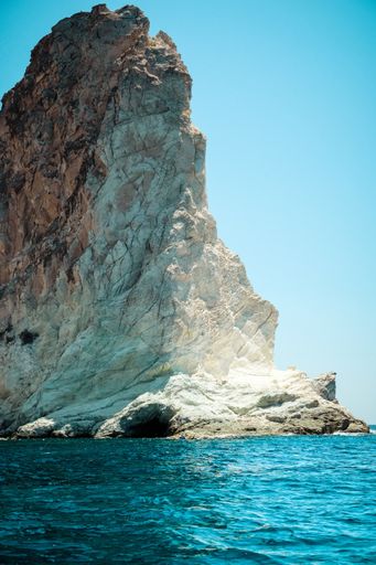 A vertical shot of a huge rock formation in the sea against the clear blue sky on a sunny summer day