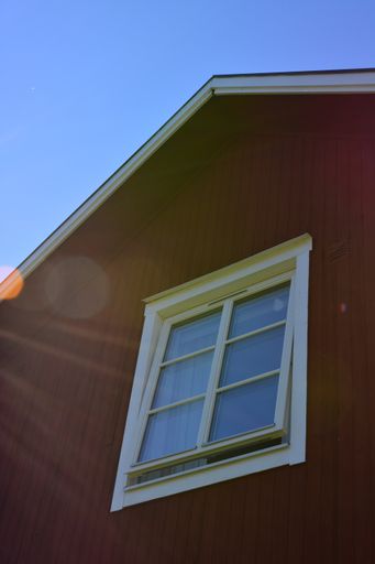 A vertical low angle shot of a traditional Scandinavian red and white house with modern windows and lens flare