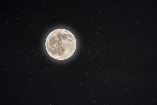 A beautiful shot of a glowing white full moon with a starry night sky in the background