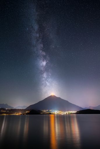 A vertical shot of the Milky Way over Lake Thun and Mount Niesen Lights over the municipality of Spiez