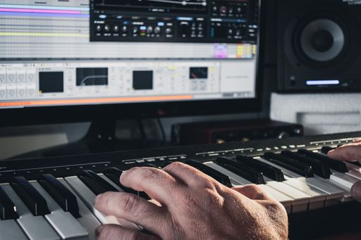 A music producer working with a midi keyboard synthesizer and a computer