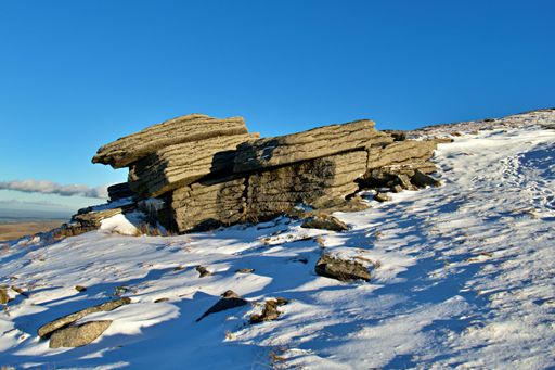 A large rock formation standing on the Yes Tor peak with an idyllic winter landscape in background
