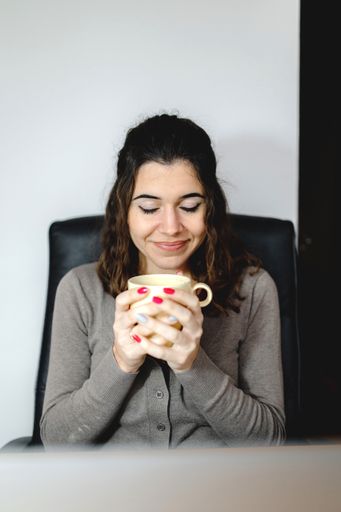 A vertical shot of a woman holding a mug in front of a laptop