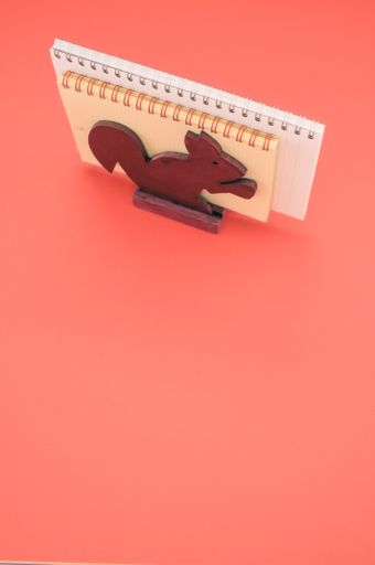 A vertical isolated shot of the notebooks in the wooden squirrel paper holder on a pink background- free space for text