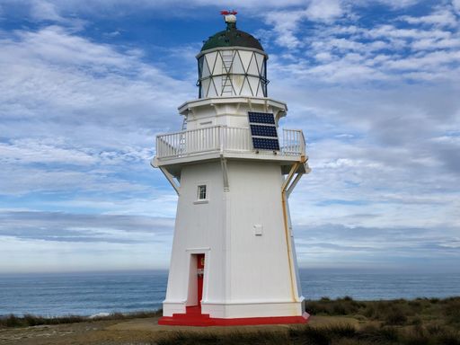 A big white lighthouse built from the stone under the cloudy sky