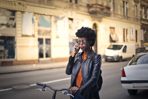 A shallow focus of a young African woman with short curly hair talking on a phone while riding a bicycle