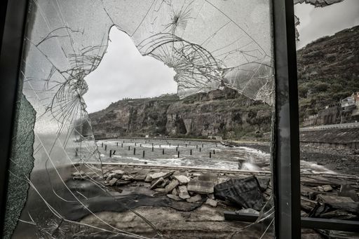 A closeup of a window with broken glass overlooking a rocky beach