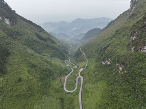 A mesmerizing curvy road passing across a valley between two large mountains covered with grass on a slightly misty day