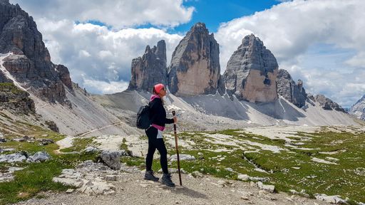 Side view of young woman standing on plateau with magnificent mountains in background. Tre Cime, Drei Zinnen, Dolomites, Dolomiti, Italy.