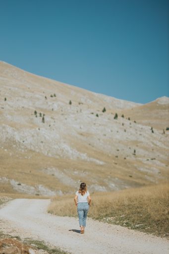 A vertical shot of a female with a t-shirt and jeans from the back on the yellow field background