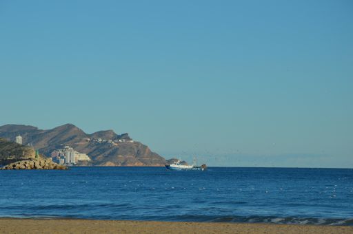 A beautiful shot of a boat in the ocean with mountains and buildings in the background