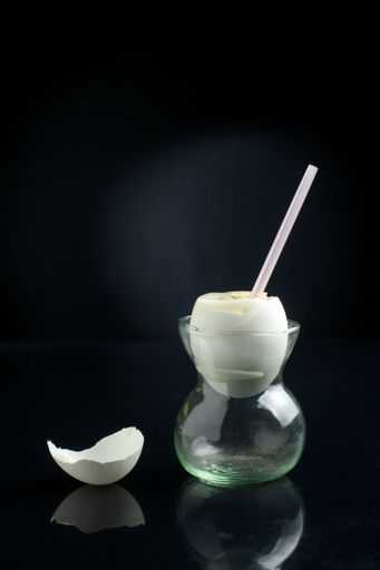 A vertical shot of a boiled egg with a straw in an egg cup and eggshell on a black background