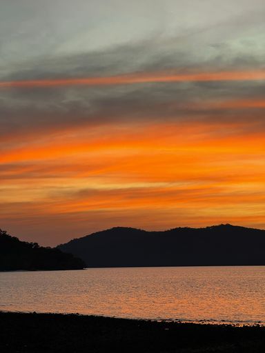 A vertical shot of the sea with silhouettes of hills at sunset.