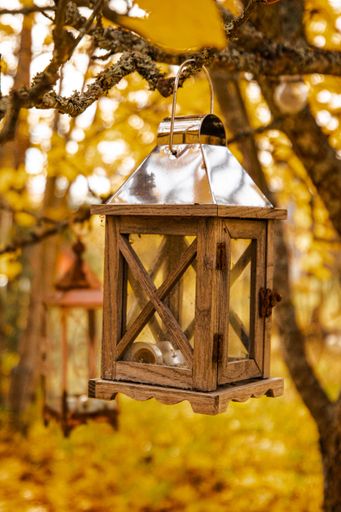 A vertical shot of a vintage decorative wooden Lantern hanging from a branch in a autumn garden