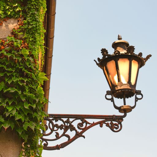 A low-angle view of a rusty vintage street lamp before the blue sky