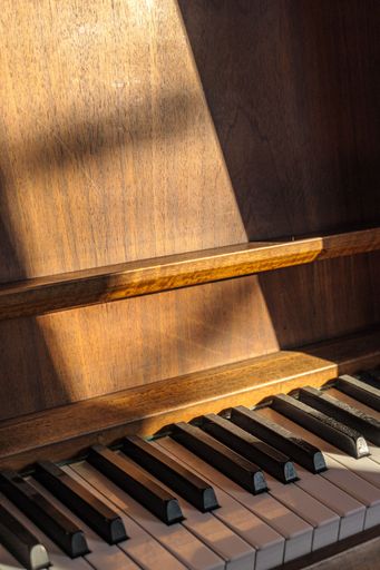 An antique upright piano standing in a bright sunlit room