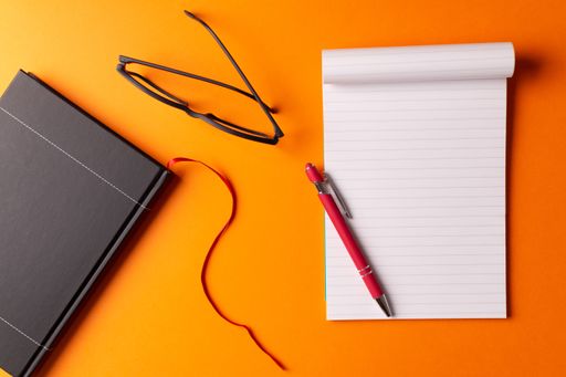 A high angle shot of a diary, an organizer, glasses, and a pen isolated on an orange background