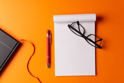 A high angle shot of a diary, an organizer, glasses, and a pen isolated on an orange background