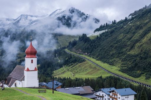 A stunning view of a rural valley in Austria, with a majestic mountain in the background and a small church perched atop its peak