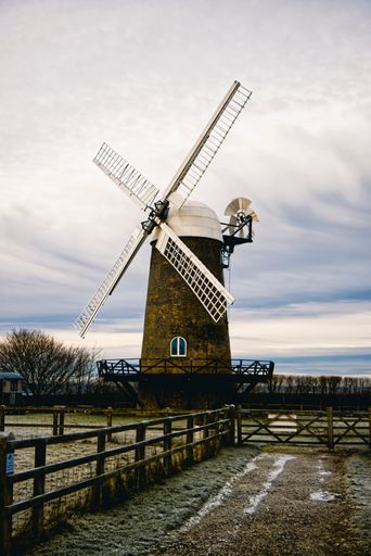 A vertical shot of a vintage windmill in the middle of a farm at a countryside