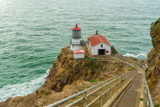 A breathtaking image of a historic lighthouse situated next to the vast ocean with a set of steps leading up to its entrance