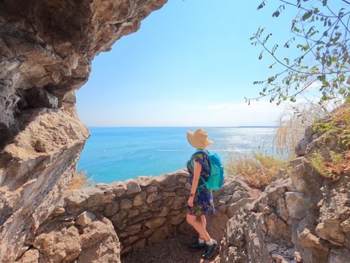 A young woman wearing a blue backpack and a hat admiring the sea view in rilkeweg, italy