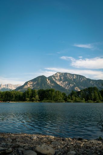 A beautiful landscape featuring a crystal clear lake surrounded by lush grass and jagged rocks, with a majestic mountain in the background