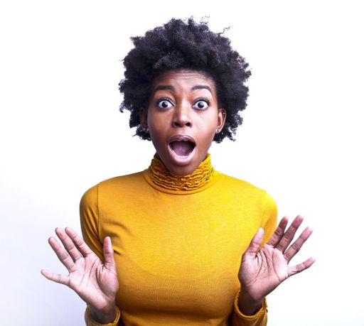 A portrait of a surprised African woman with short curly hair wearing a yellow turtleneck against a white background
