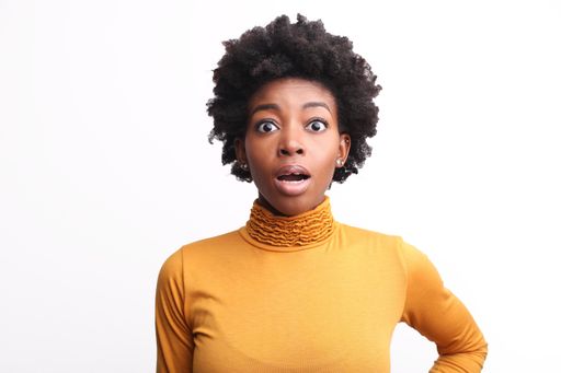 A portrait of a scared and shocked African woman with short curly hair against a white background