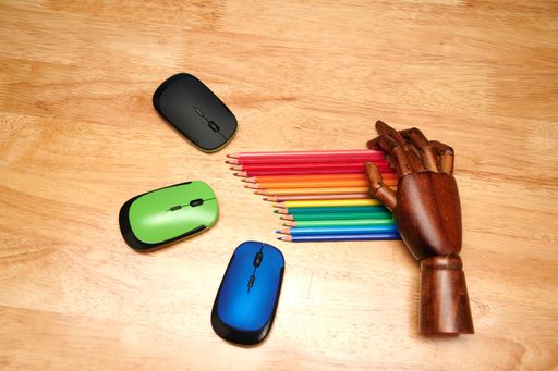 A top view of  multi-colored pencils, computer mouses with an articulated wooden hand